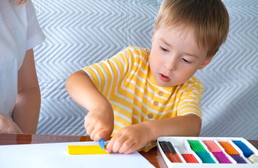 Child kid boy play colorful plasticine at kindergarten or at home. Mother and son or babysitter are engaged in early development, preparation for school. Selective focus.